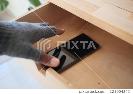 Hand with gloves stealing a for smartphone in wooden drawer  125004243