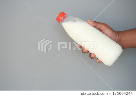 Holding a bottle of fresh milk against a neutral background Holding a bottle of fresh milk against a neutral background 125004244