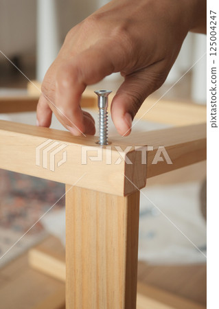 Building a wooden table with a hand tightening a screw 125004247