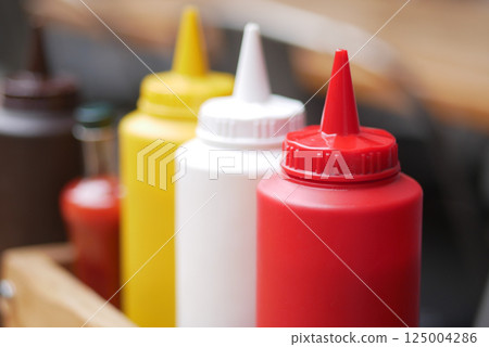Colorful condiment bottles lined up on a rustic wooden table Colorful condiment bottles lined up on a rustic wooden table 125004286