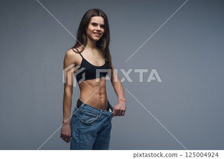 Woman with perfect body demonstrates weight loss, slimming by wearing old big jeans 125004924