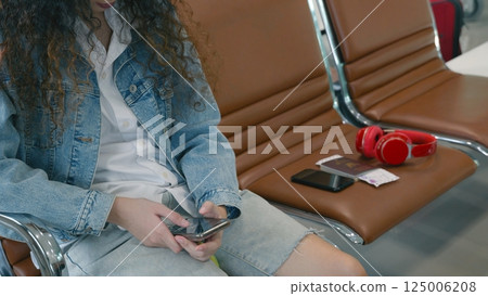 Passenger traveler woman in airport gate play smartphone for waiting air vacation travel, hipster female sitting and using mobile phone in terminal hall area while waiting for her traveling flight Passenger traveler woman in airport gate play smartphone for waiting air vacation travel, hipster female sitting and using mobile phone in terminal hall area while waiting for her traveling flight 125006208