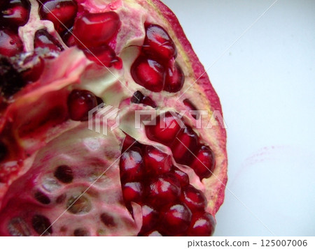 Close-up of a ripe pomegranate cut open to reveal juicy red seeds and textured interior against a light background. High quality photo 125007006