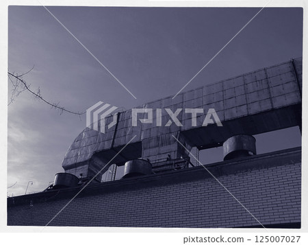 Large metallic ducts are positioned on the roof of a brick building, contrasting with the clear blue sky. The structure highlights industrial architecture and urban design. 125007027