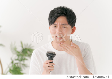 A young man shaving his beard 125008751