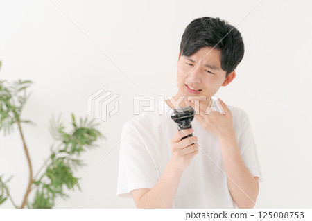 A young man shaving his beard 125008753