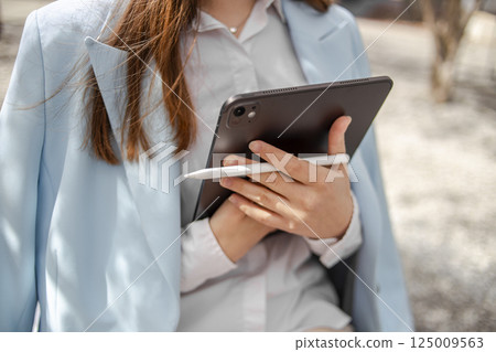 Woman using a tablet with a digital pen outdoors Woman using a tablet with a digital pen outdoors 125009563
