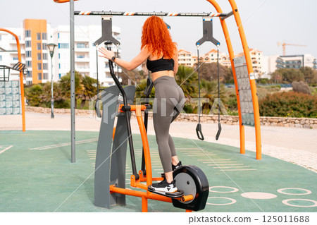 Fit woman exercising on elliptical cross trainer 125011688