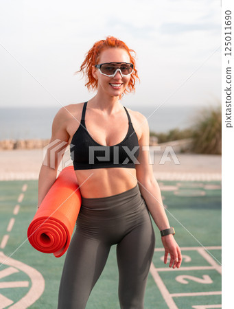 Smiling redhead woman with yoga mat in summer park Smiling redhead woman with yoga mat in summer park 125011690