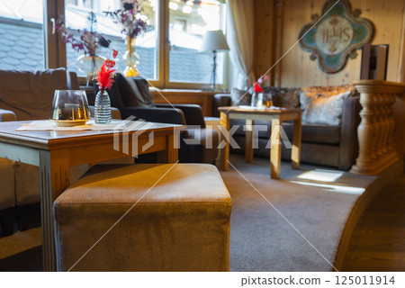 Cozy lounge featuring wooden furniture, cushioned chairs, floral vases, and large windows with rooftop views, set in an upscale alpine retreat in Ischgl, Austria. Cozy lounge featuring wooden furniture, cushioned chairs, floral vases, and large windows with rooftop views, set in an upscale alpine retreat in Ischgl, Austria. 125011914