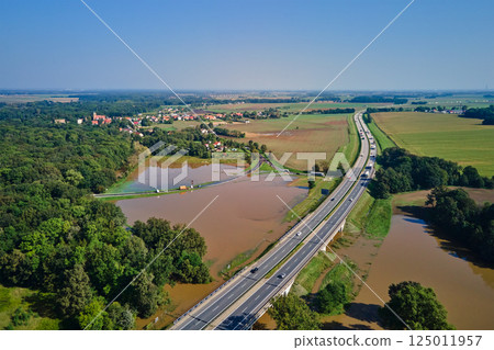 Aerial view of flooded fields and submerged rural road near busy highway. Concept of climate impact, transportation disruption and natural disaster Aerial view of flooded fields and submerged rural road near busy highway. Concept of climate impact, transportation disruption and natural disaster 125011957