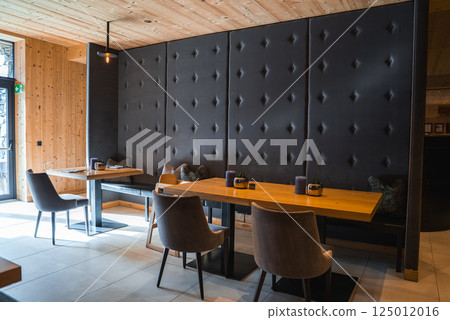 Elegant dining space with wooden walls, tufted leather panel, gray chairs, and natural light from a glass door, located in the Italian Alps. 125012016