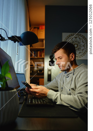 Tired freelancer procrastinating at home office, scrolling phone instead of working. Unproductive man using smartphone at home desk. Concept of procrastination and distraction in remote work Tired freelancer procrastinating at home office, scrolling phone instead of working. Unproductive man using smartphone at home desk. Concept of procrastination and distraction in remote work 125012066