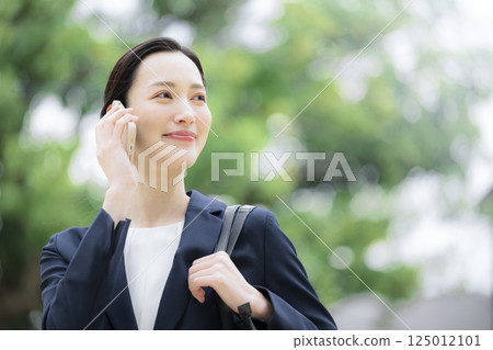 A woman in a business suit talking on her smartphone outdoors in the fresh greenery and looking up. Close-up of an image of sales and outside work 125012101