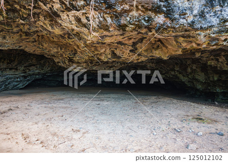 Shallow cave entrance with a rugged rock ceiling, sandy ground, and hanging vines. Likely located on Kauai, showcasing natural geological features. 125012102