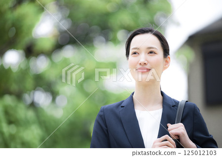 A woman wearing a business suit outdoors with fresh greenery, looking like she is doing sales or going out 125012103