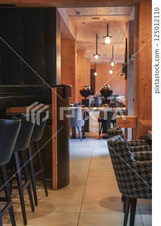 Dining area of a luxury hotel in the Italian Alps featuring natural wood walls, pendant lighting, black leather stools, and houndstooth patterned chairs. Dining area of a luxury hotel in the Italian Alps featuring natural wood walls, pendant lighting, black leather stools, and houndstooth patterned chairs. 125012110