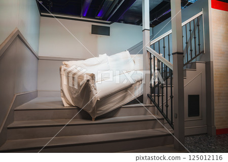 A white couch is positioned on a staircase with a wooden railing, part of a Friends themed exhibition in London, replicating a famous TV scene. 125012116