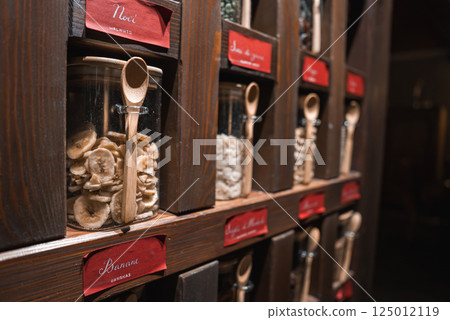 Neatly arranged wooden shelf with glass jars of dried goods, labeled in Italian, featuring small wooden spoons and warm lighting in a luxury setting. Neatly arranged wooden shelf with glass jars of dried goods, labeled in Italian, featuring small wooden spoons and warm lighting in a luxury setting. 125012119