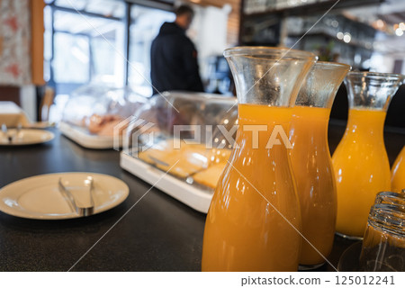 Breakfast buffet featuring carafes of orange juice, covered food trays, and modern decor. Large windows reveal natural light in a mountain setting. Breakfast buffet featuring carafes of orange juice, covered food trays, and modern decor. Large windows reveal natural light in a mountain setting. 125012241