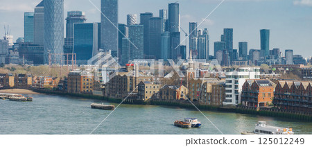 Aerial perspective of London's Canary Wharf skyline with modern skyscrapers, the River Thames, historic brick buildings, and boats on the water. 125012249