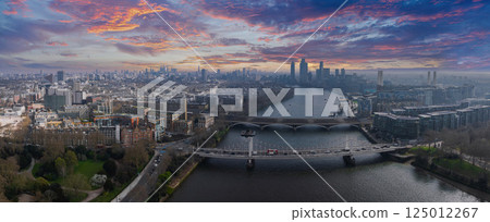 Aerial view of London featuring the River Thames, Chelsea and Albert Bridges, Canary Wharf, the Shard, green park spaces, and urban architecture. 125012267