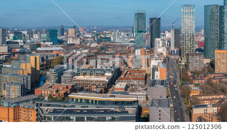 Aerial view of Manchester, UK, featuring Beetham Tower, modern skyscrapers, historic buildings, busy roads, and a clear blue sky on a sunny day. 125012306