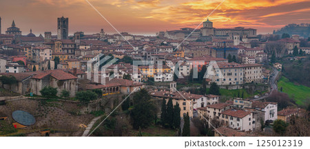 The old town of Bergamo, Italy, features Torre del Gombito, the Basilica of Santa Maria Maggiore, terracotta rooftops, and rolling hills at sunset. 125012319