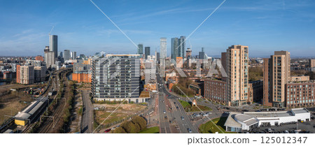 Aerial view of Manchester, UK, featuring Beetham Tower, modern skyscrapers, traditional architecture, roads, railways, and a curved white roofed structure. Aerial view of Manchester, UK, featuring Beetham Tower, modern skyscrapers, traditional architecture, roads, railways, and a curved white roofed structure. 125012347