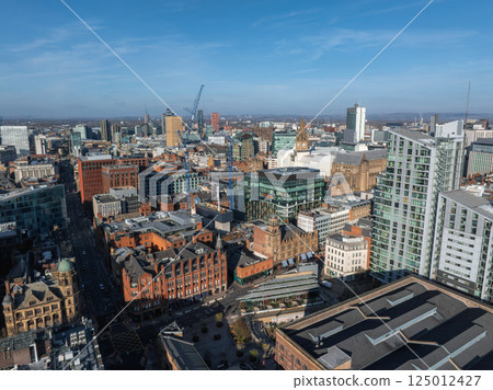 Aerial view of Manchester, UK, on a sunny day with skyscrapers, Beetham Tower, red brick buildings, and construction cranes in the city center. Aerial view of Manchester, UK, on a sunny day with skyscrapers, Beetham Tower, red brick buildings, and construction cranes in the city center. 125012427