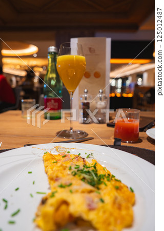 Close up of a plate with a herb garnished omelet, orange juice, and sparkling water on a wooden table in a modern, upscale dining area in Austria. 125012487