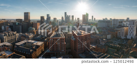 Aerial view of Manchester, UK, on a sunny day, featuring skyscrapers, construction cranes, historic brick buildings, and modern architecture. Aerial view of Manchester, UK, on a sunny day, featuring skyscrapers, construction cranes, historic brick buildings, and modern architecture. 125012498