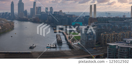 Aerial perspective of London with the River Thames, Battersea Power Station, modern skyscrapers of Canary Wharf, railway tracks, and a docked boat. Aerial perspective of London with the River Thames, Battersea Power Station, modern skyscrapers of Canary Wharf, railway tracks, and a docked boat. 125012502