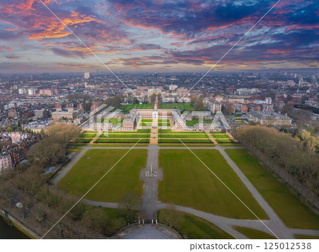 Aerial perspective of the Royal Hospital Chelsea in London, featuring red brick buildings, green lawns, and the urban sprawl under a cloudy sky. 125012538
