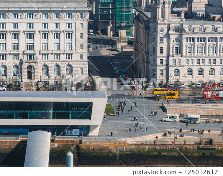 Aerial view of Liverpool showcasing the Three Graces, Museum of Liverpool, waterfront, and vibrant street activity with buses and pedestrians. 125012617