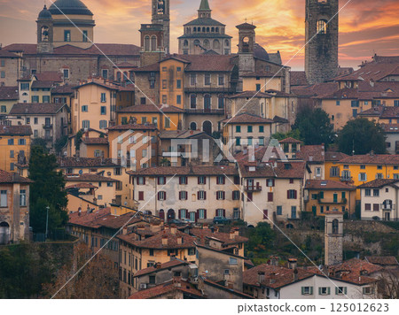 View of Bergamo's old town in Italy during sunset, featuring the Basilica of Santa Maria Maggiore, Campanone bell tower, and terracotta roofed buildings. 125012623
