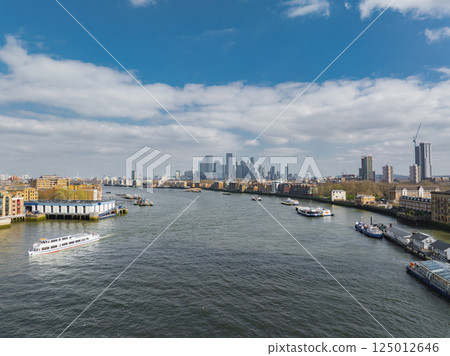 Aerial view of the River Thames in London with boats, modern and historic buildings, Canary Wharf skyline, and a construction crane visible. Aerial view of the River Thames in London with boats, modern and historic buildings, Canary Wharf skyline, and a construction crane visible. 125012646