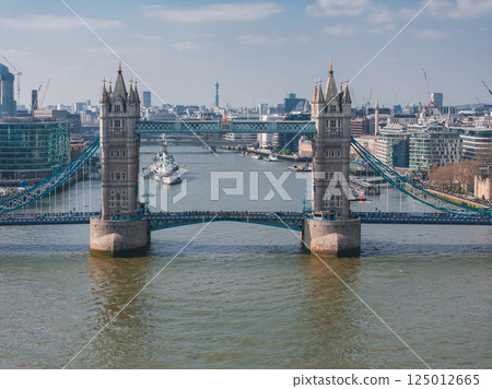 Tower Bridge's iconic towers and blue suspension elements span the River Thames, with HMS Belfast, BT Tower, and London's skyline in the background. Tower Bridge's iconic towers and blue suspension elements span the River Thames, with HMS Belfast, BT Tower, and London's skyline in the background. 125012665