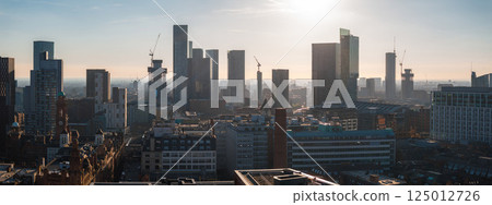Aerial view of Manchester, UK, on a sunny day showing modern skyscrapers, historic architecture, cranes, and urban development in the city center. 125012726