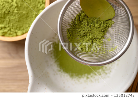 Matcha green tea powder pouring in sieve prepare for tea mixing, Top view Matcha green tea powder pouring in sieve prepare for tea mixing, Top view 125012742