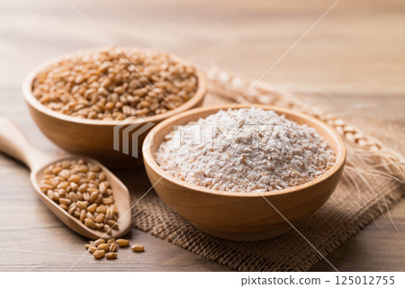 Whole wheat flour with wheat grain in bowl on wooden background 125012755