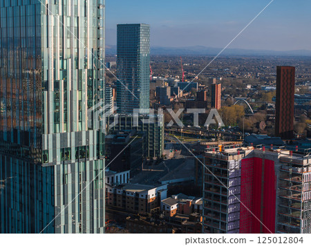 Aerial view of Manchester, UK, on a sunny day with skyscrapers, modern and traditional architecture, construction activity, and suburban areas in the distance. Aerial view of Manchester, UK, on a sunny day with skyscrapers, modern and traditional architecture, construction activity, and suburban areas in the distance. 125012804
