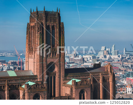 Aerial view of Liverpool showcasing the Gothic Revival Liverpool Cathedral, modern buildings, the Royal Liver Building, and a clear blue sky with a contrail. 125012820