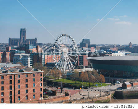 Aerial view of Liverpool featuring the Liverpool Cathedral, the Wheel of Liverpool, the MandS Bank Arena, and historic Albert Dock buildings under a clear sky. Aerial view of Liverpool featuring the Liverpool Cathedral, the Wheel of Liverpool, the MandS Bank Arena, and historic Albert Dock buildings under a clear sky. 125012823