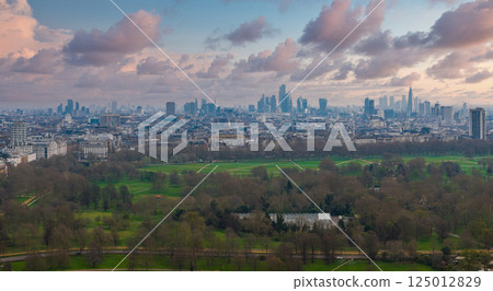 Aerial perspective of London featuring The Shard, City of London skyscrapers, and Hyde Park's green expanse under an overcast sky. 125012829