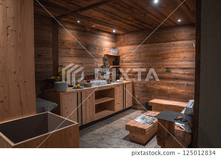 Cozy interior featuring wooden walls, stone flooring, a refreshment area with a silver dispenser, fresh fruit, and a small seating area with a bench. 125012834