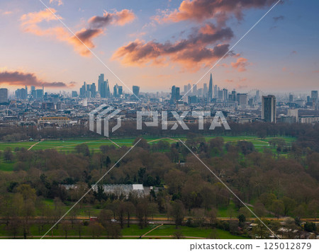 Aerial view of London featuring The Shard, Canary Wharf skyscrapers, and a large green park bordered by trees under an overcast sky. Aerial view of London featuring The Shard, Canary Wharf skyscrapers, and a large green park bordered by trees under an overcast sky. 125012879