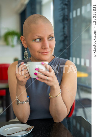 Young woman with cancer sitting in a cafe, drinking coffee and enjoying everyday life. The concept highlights that people with illnesses continue to live actively and socialize 125013831