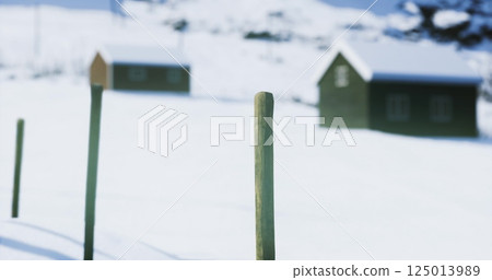 Snow covered landscape with rustic houses and wooden posts on a winter day Snow covered landscape with rustic houses and wooden posts on a winter day 125013989