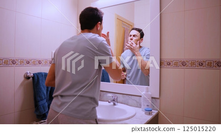 Man applying cocoa lip balm in bathroom mirror Man applying cocoa lip balm in bathroom mirror 125015220